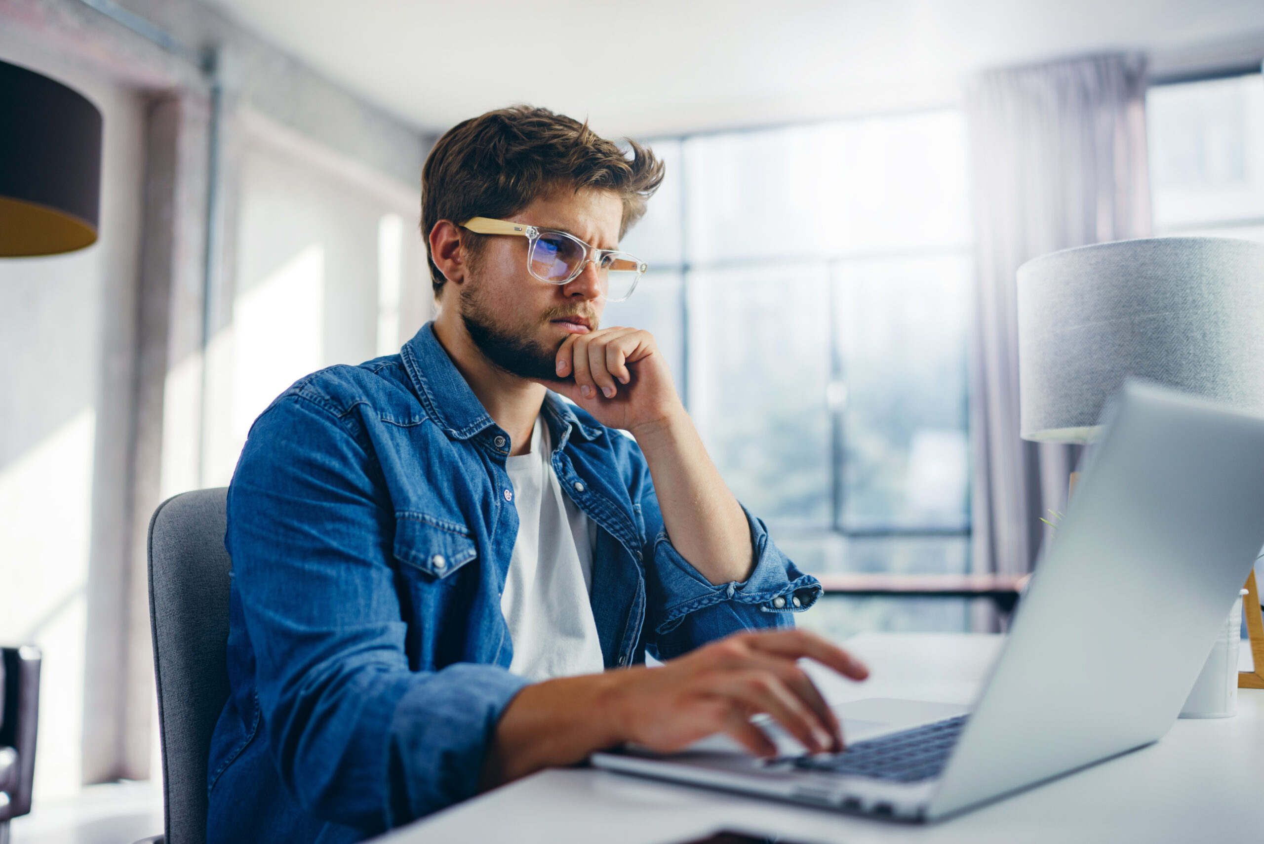 Young man typing on laptop. Modern businessman at sunny office. Freelancer at work. Blogger or journalist writing new article